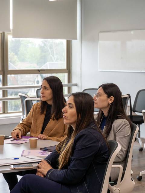 Varias mujeres sentadas en una sala de reuniones escuchando atentamente.