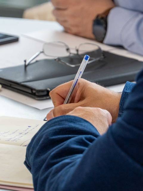 Una persona escribe en un cuaderno mientras otra está sentada a su lado.