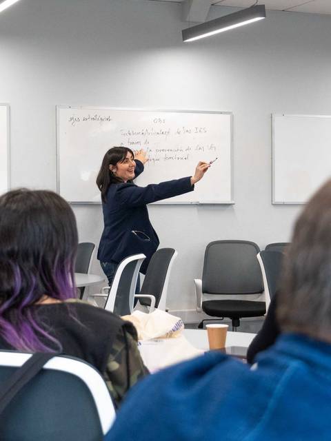 Una mujer está dando una presentación en una sala de clases mientras la audiencia la observa.