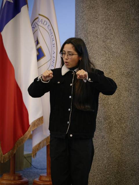 Una persona se expresa mientras se encuentra en un escenario con banderas de fondo.