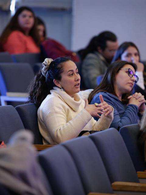 Una mujer levantando la mano durante una charla en un auditorio lleno de personas.