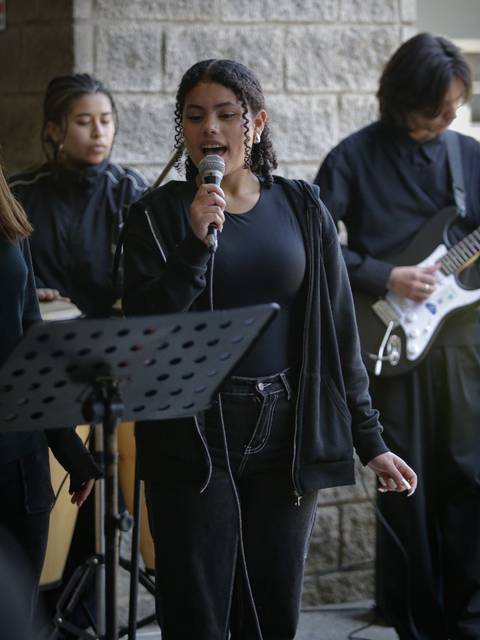 Un grupo de jóvenes está actuando en un escenario, con una cantante principal que sostiene un micrófono.