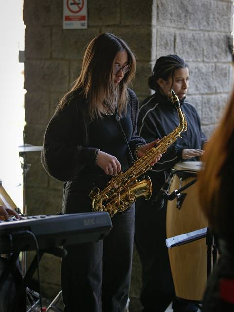 Una joven tocando el saxofón en un contexto musical con otros músicos a su alrededor.