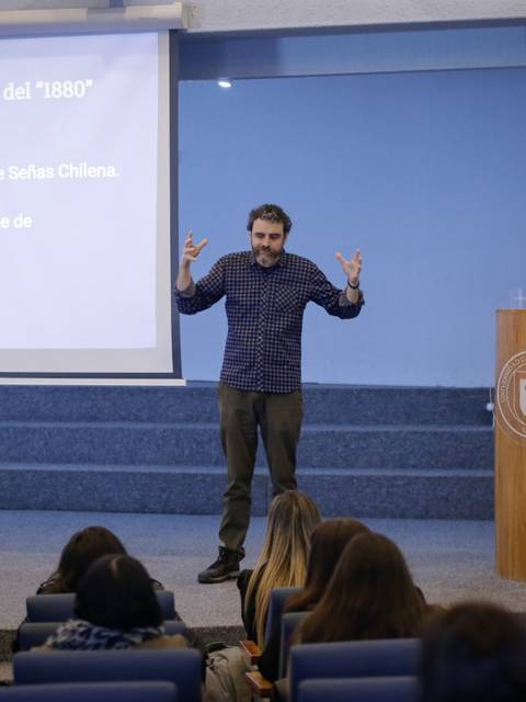 Un conferencista está presentando sobre la lengua de los Selk'nam en un auditorio con una audiencia atenta.