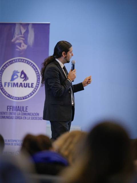 Un hombre vestido de traje está hablando en un evento mientras sostiene un micrófono.