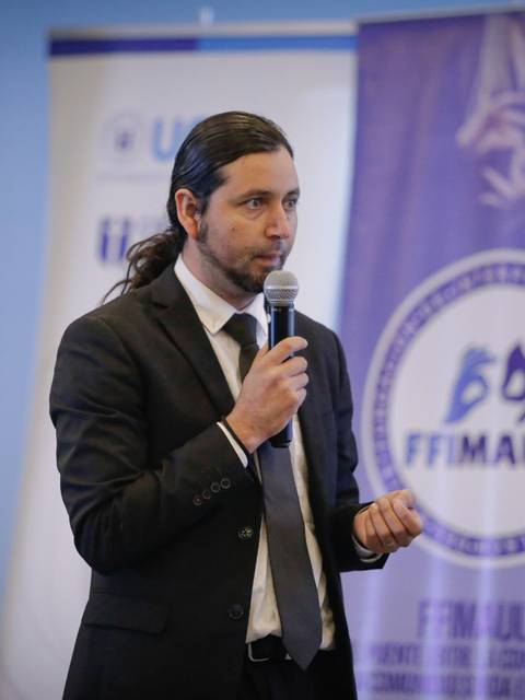 Un hombre de pie, vestido de traje, habla al micrófono durante una presentación.
