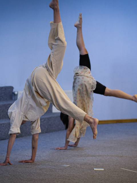Dos personas realizando acrobacias en una sala con fondo azul.