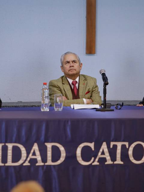 Tres hombres se encuentran sentados en una mesa durante un evento en la Universidad Católica.