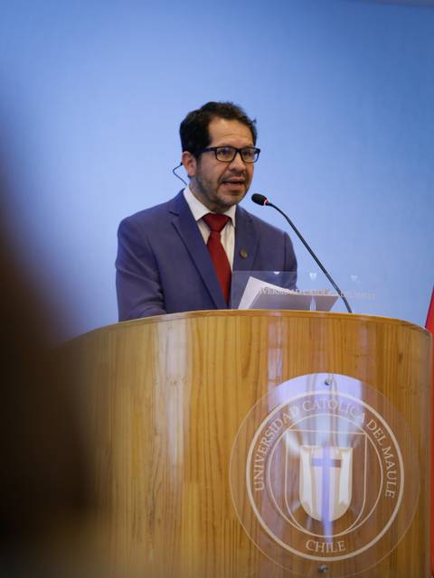 Un hombre con gafas habla en un podio de madera durante un evento académico.