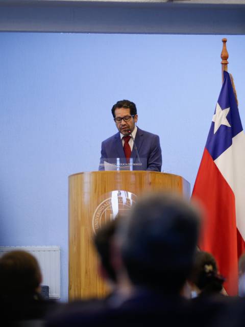 Un orador está presentando en un evento con banderas chilenas de fondo.