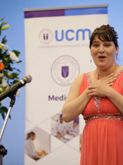 Una mujer vestida con un vestido rosa se presenta ante un micrófono en un evento, mostrando una expresión de emoción.