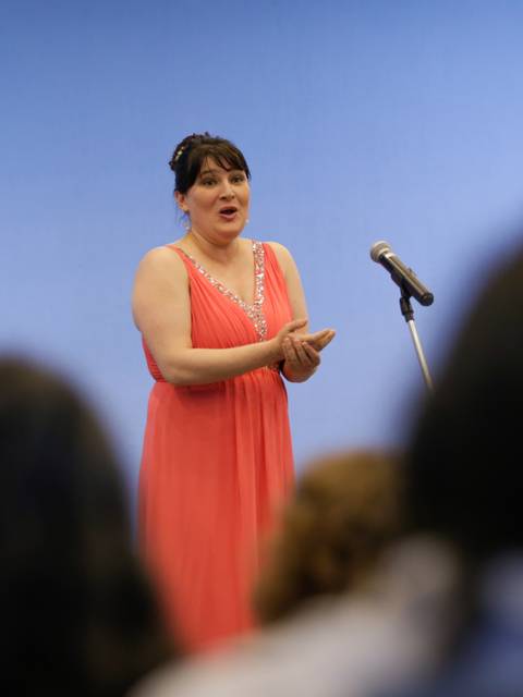 Una mujer canta en un escenario mientras el público la observa.