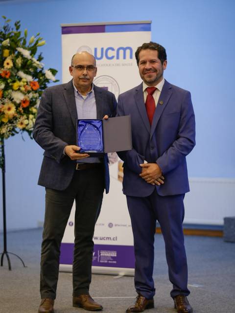Dos hombres posan juntos mientras uno sostiene un premio en un evento formal.