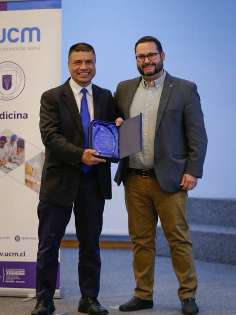 Dos hombres sonrientes durante una ceremonia de entrega de un reconocimiento.