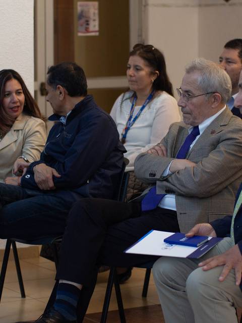 Un grupo de personas sentadas en una sala, conversando y prestando atención a una presentación.
