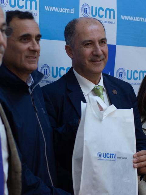 Cuatro personas posan juntas sosteniendo una bolsa con el logo de la UCM en un evento.