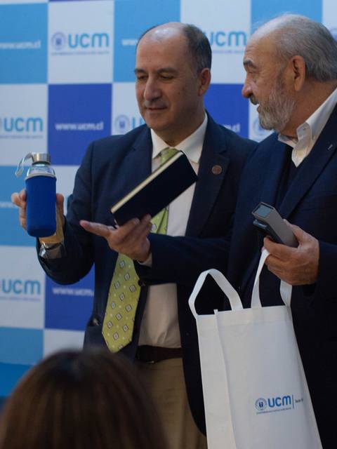 Dos hombres sostienen objetos en un evento formal.