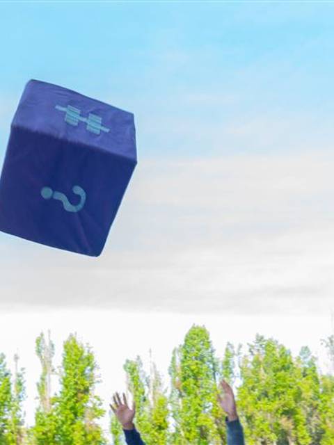 Una persona lanza una caja con un signo de interrogación al aire en un entorno natural.