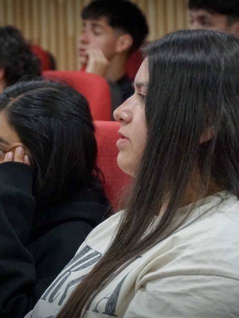 Un grupo de jóvenes está sentado en un auditorio, escuchando atentamente.