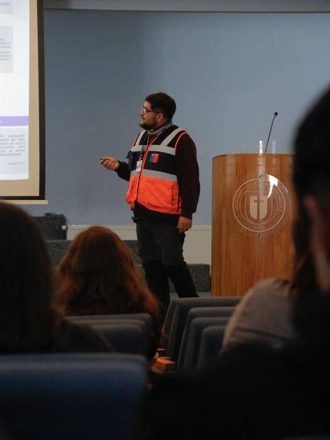 Un hombre presenta un tema frente a una audiencia en un auditorio.