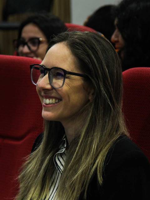 Una mujer sonriente con gafas sentada en un auditorio.