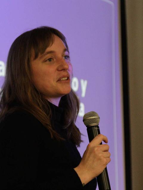 Una mujer está dando una presentación frente a una pantalla con texto.
