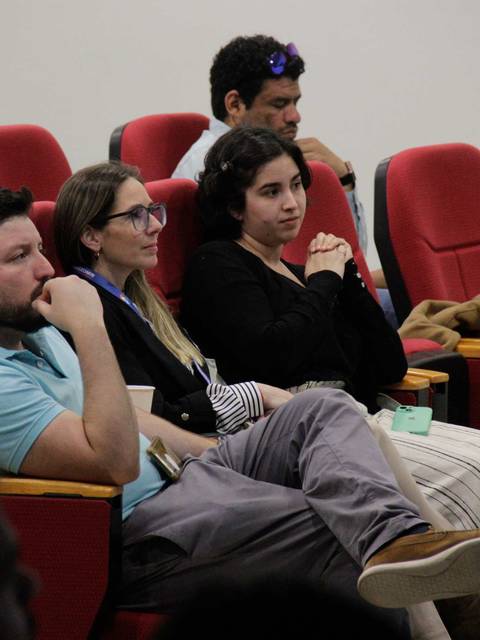 Un grupo de personas sentadas en una sala, prestando atención a una presentación.