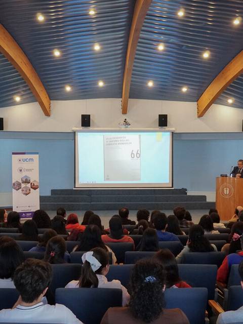 Una conferencia con un ponente en el escenario y una audiencia prestando atención.