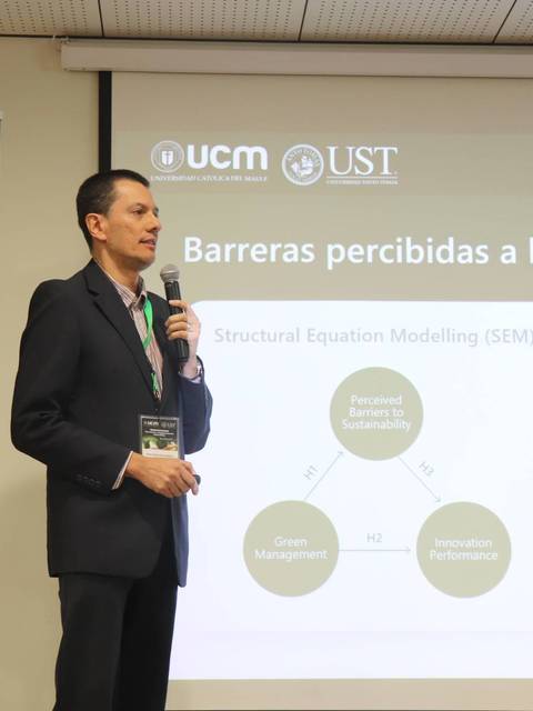 Un presentador expone sobre las barreras percibidas a la sostenibilidad en un evento académico.