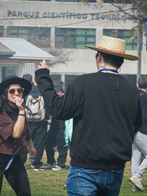 Un grupo de personas se divierte al aire libre en un parque mientras una mujer y un hombre bailan entre risas.