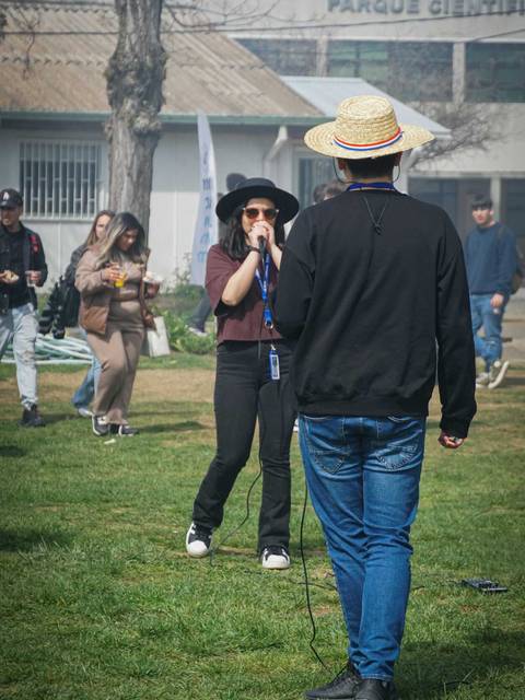 Un grupo de personas se reúne en un parque mientras una persona canta frente a otra que la escucha.