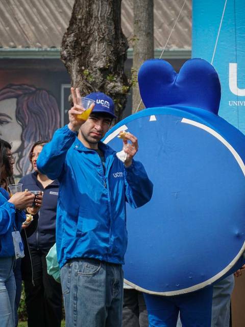 Un grupo de personas vestidas de azul posan junto a una figura grande de color azul en un evento universitario.