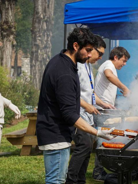 Un grupo de personas cocinando a la parrilla en un evento al aire libre con viento y humo alrededor.