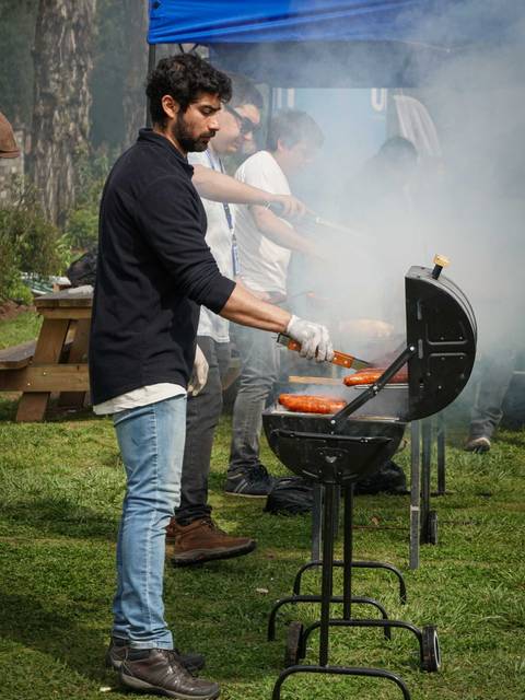Un hombre cocina en una parrilla al aire libre mientras una columna de humo se eleva alrededor de él.