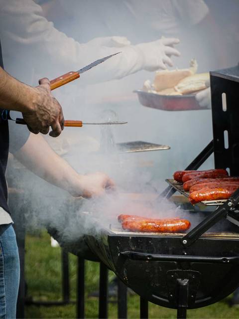 Una persona está asando salchichas en una parrilla rodeada de humo.
