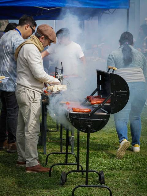 Un grupo de personas disfrutando de una parrillada al aire libre con humo y carne asándose.