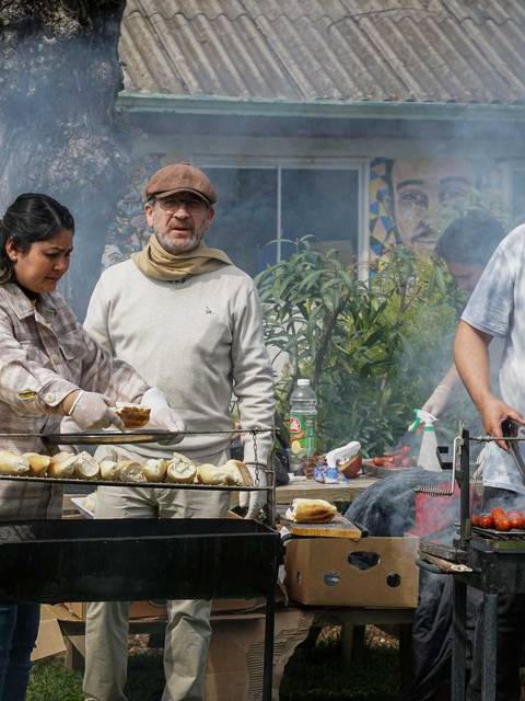 Un grupo de personas cocina al aire libre, rodeadas de humo, mientras preparan alimentos en parrillas.