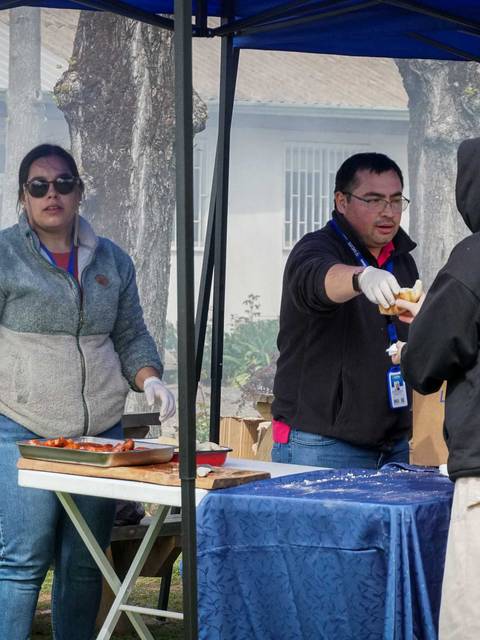 Un grupo de personas interactuando en un evento al aire libre, con una mesa de comida y una carpa.