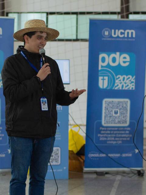 Un hombre y una mujer están hablando en un evento mientras se encuentran frente a unos carteles de la universidad.