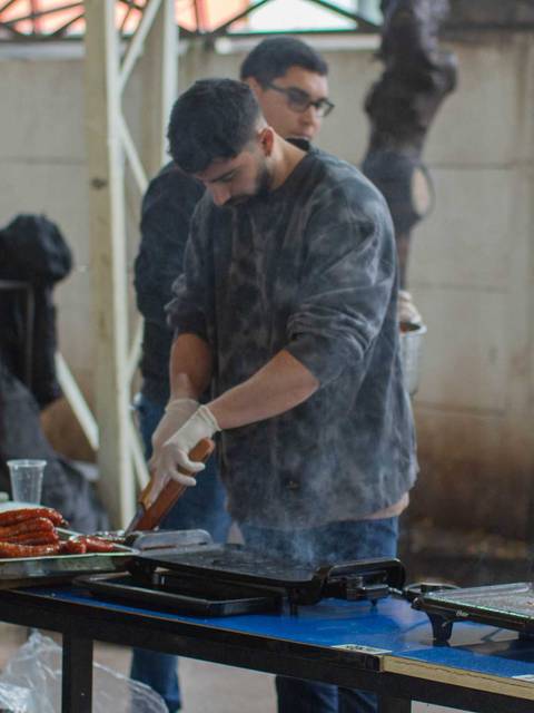 Una persona está cocinando en una parrilla al aire libre mientras otra observa.