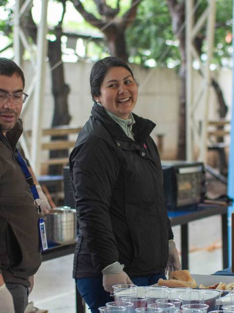 Un grupo de personas sonrientes en un evento, sirviendo comida y bebida en una mesa.