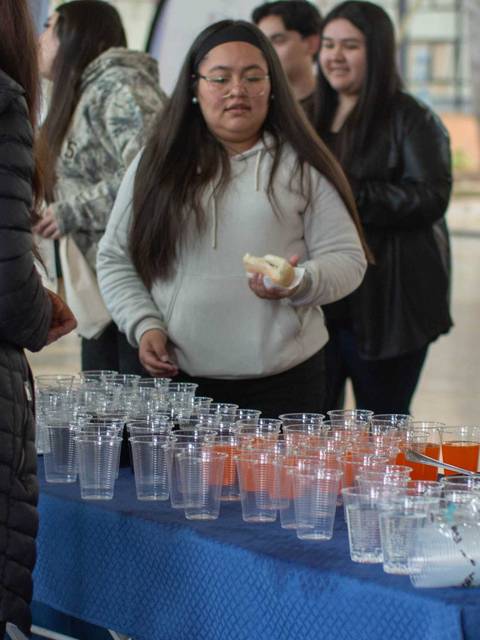 Un grupo de personas en un evento social, con una mesa llena de vasos y bebidas en un ambiente interior.