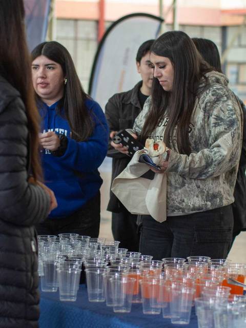 Un grupo de personas interactuando en un evento mientras se sirven bebidas en vasos de plástico.