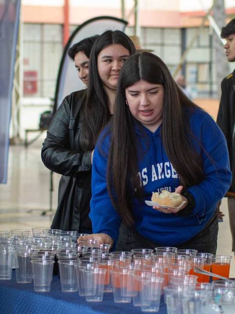 Un grupo de jóvenes está interactuando en un evento, mientras una persona observa un montón de vasos transparentes en una mesa.
