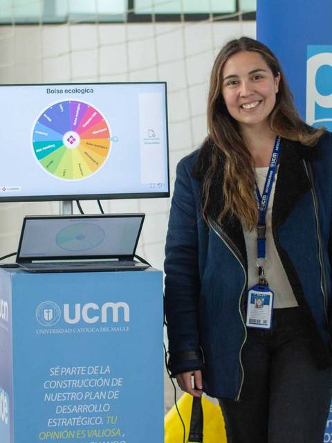 Una joven sonriente pose frente a un stand con gráficos y letreros institucionales.