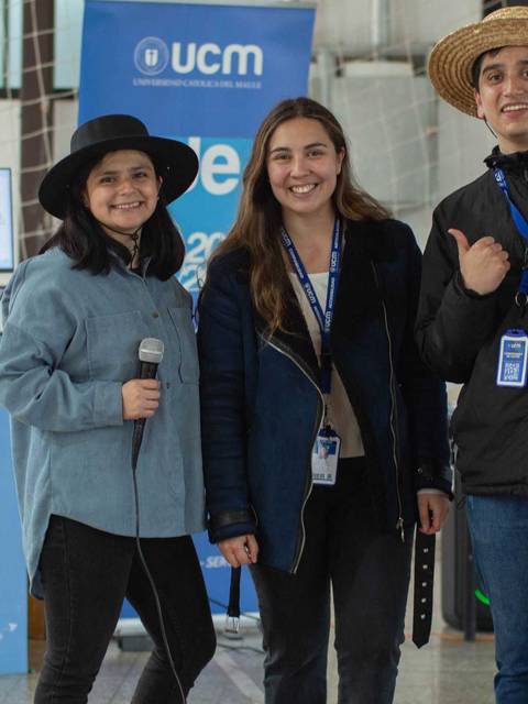 Un grupo de tres personas sonrientes posan con micrófonos en un evento universitario.