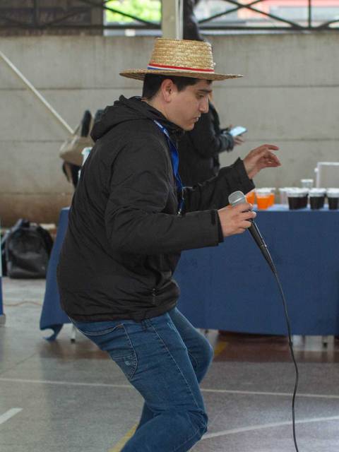 Un joven con sombrero de paja canta mientras se presenta en un evento en un gimnasio.
