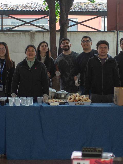 Un grupo de personas sonrientes se presenta frente a una mesa con bebidas y alimentos en un evento al aire libre.