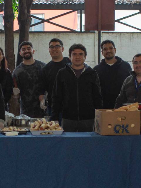 Grupo de personas posando delante de una mesa con comida y bebidas en un ambiente al aire libre.