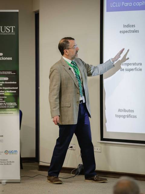 Un presentador señala una diapositiva mientras habla sobre temas relacionados con índices espectrales y atributos topográficos.